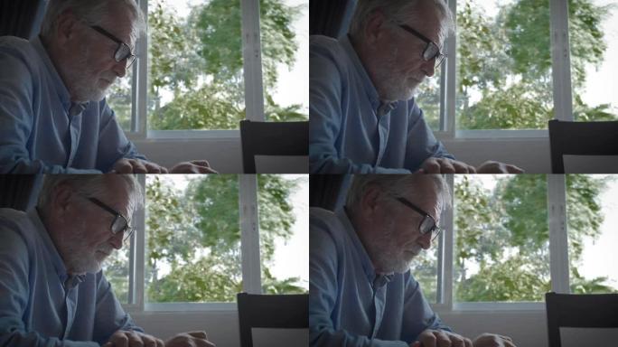 祖父或高级男子坐在窗户附近阅读合同或文件