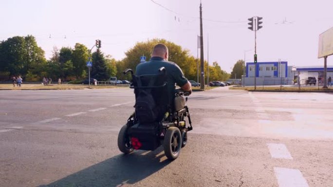 轮椅男子。残疾人。一名坐在自动轮椅上的年轻残疾人在人行横道过马路。后视图