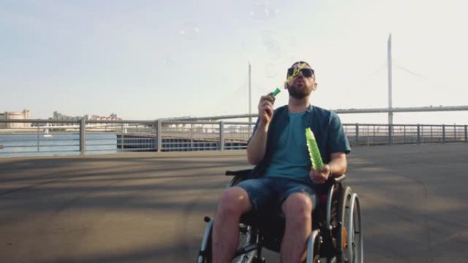 戴着太阳镜的年轻人坐在轮椅上吹着肥皂泡在城市堤防上，失去了自信。