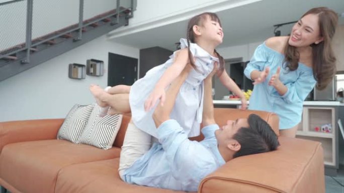 亚洲家庭与父亲强大的时尚父亲抛出他兴奋的女儿让飞机大喊大叫有很多精力，快乐，就像这个游戏在家里的客厅
