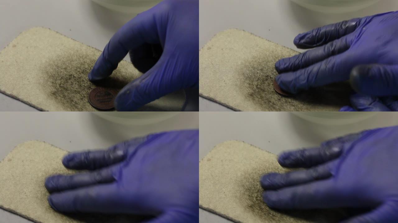 一个戴着橡胶手套的人在毛毡上擦了一个用硫磺软膏制成的铜币。显示解脱。
