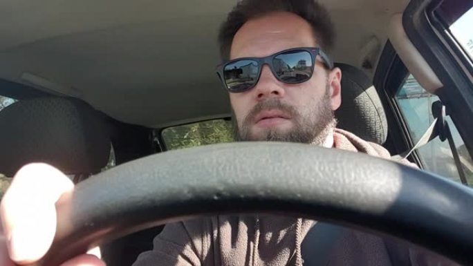 戴眼镜的大胡子男子开车，用智能手机相机自拍