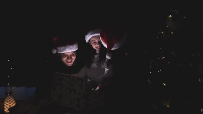 年轻的家庭父亲，母亲和女孩打开礼品盒并发出灯光
