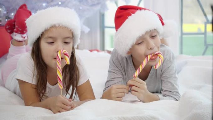 穿着睡衣的可爱兄妹的视频在冬天的早晨舔圣诞糖果。