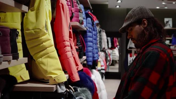 男人在寒假期间在商店里看衣服。他去购物，我们可以找到冬装。非常适合去4K山里滑雪