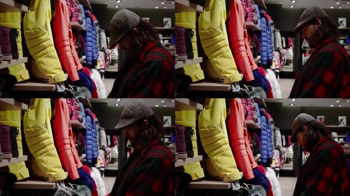 男人在寒假期间在商店里看衣服。他去购物，我们可以找到冬装。非常适合去4K山里滑雪