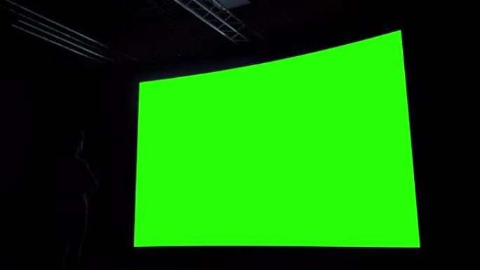 女人在黑暗的房间里看着大的空白绿色屏幕 -- 色度键概念