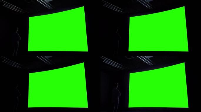 女人在黑暗的房间里看着大的空白绿色屏幕 -- 色度键概念