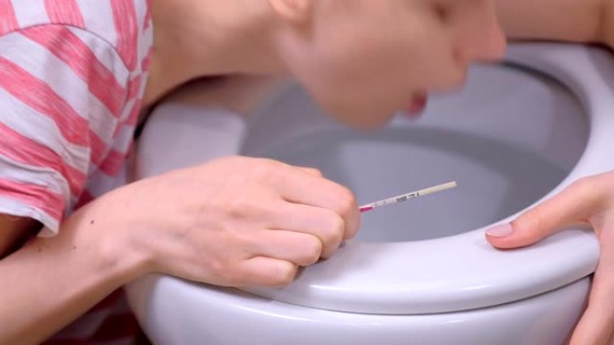 晨吐。手握妊娠试验的年轻孕妇正在家中厕所呕吐，特写视图。