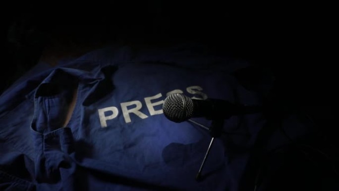 新闻自由和新闻概念。蓝色记者背心在黑暗中与背光和雾。麦克风和手铐。有选择性的重点