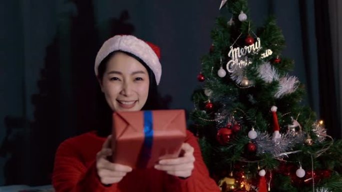 戴红帽子的亚洲女人送礼盒，在客厅说 “新年快乐” 和 “圣诞节”