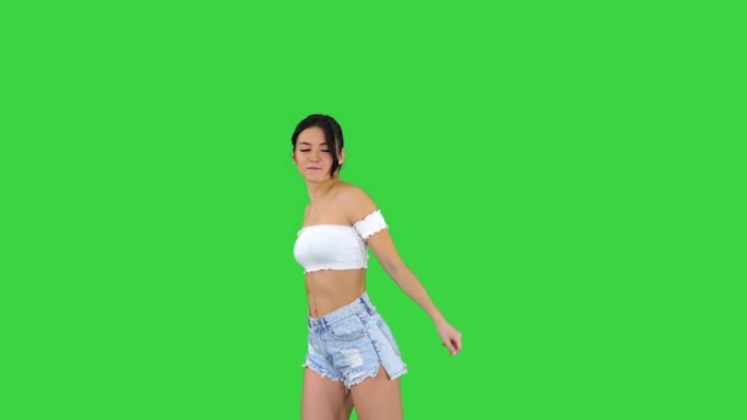 可爱的西班牙裔女模特穿着牛仔短裤在绿屏上跳舞，色键