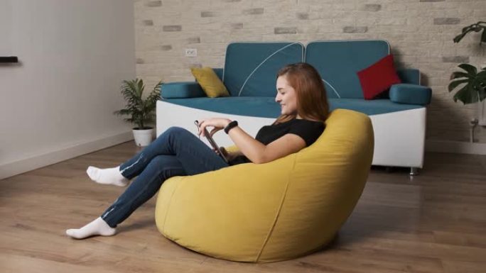 女人坐在一个黄色的豆袋上，用平板电脑与朋友聊天