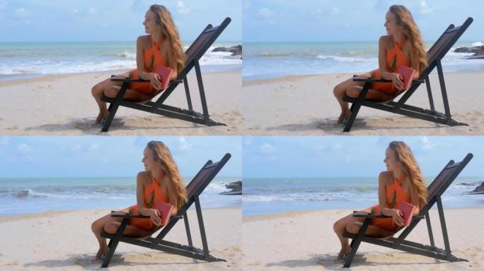 金发女孩坐在海洋海滩的折叠椅上