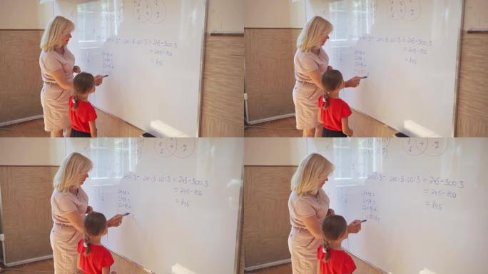 善良成熟的小学老师向她的女学生展示如何在白板上解决数学问题
