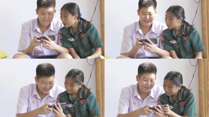 快乐的亚洲小学生和他穿着校服的妹妹在上学前正在智能手机上玩网络游戏。