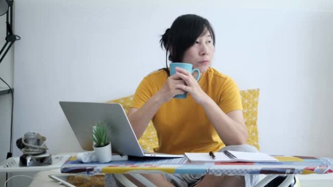 新型冠状病毒肺炎期间，亚洲女性在熨衣板上使用笔记本电脑或在家工作。
