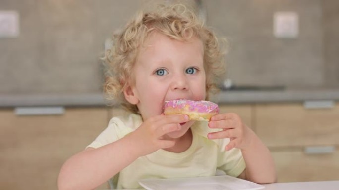 可爱的小女孩向左看，然后坐在厨房的桌子旁，从盘子里拿一个甜甜圈咬一口
