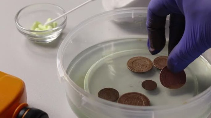 一名男子将铜币放入装有磷酸的容器中，以进行额外的清洁和去除腐蚀残留物。