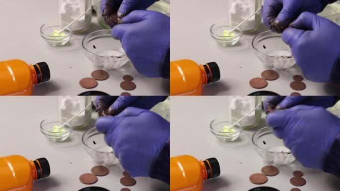 一个人用一稀水和苏打水清洗铜币。附近有一种用于青铜色的硫酸软膏。