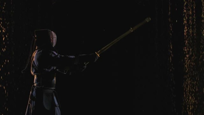 日本剑道战士的侧视图，用竹剑和传统服装在雨滴中的黑色背景下进行训练。特写。慢动作