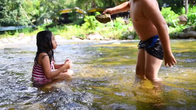 两个玩耍的孩子在河边把石头放进水里。快乐和游戏概念