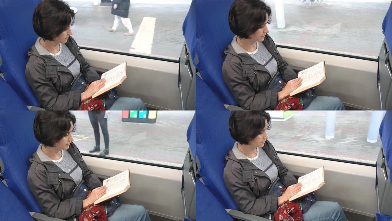 白人妇女坐在窗边的火车上看书，火车停在平台上