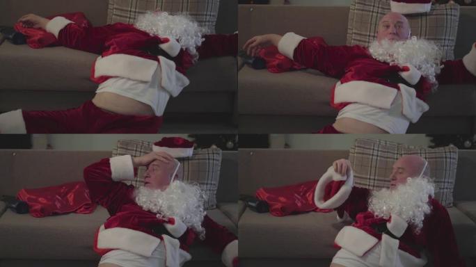 穿着圣诞老人服装的醉酒老人假白胡子，从床上掉下来，四处张望。坏圣诞老人。酗酒、抑郁、消极主义、孤独