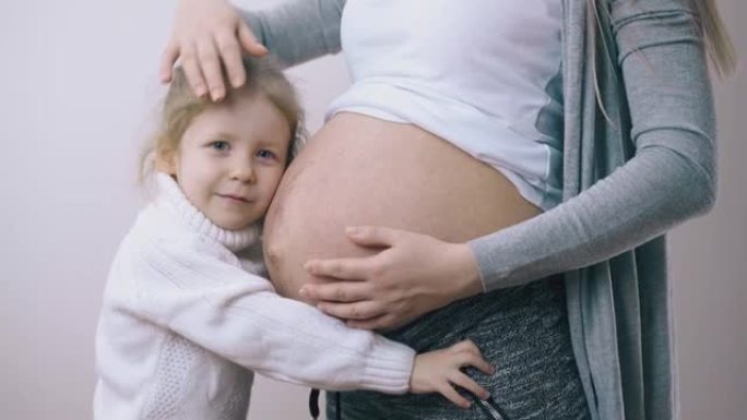 小孩拥抱怀孕的妈妈在白墙露出肚子