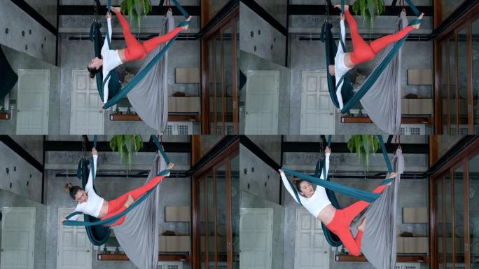 成年运动女性挂在吊床上进行飞行瑜伽。