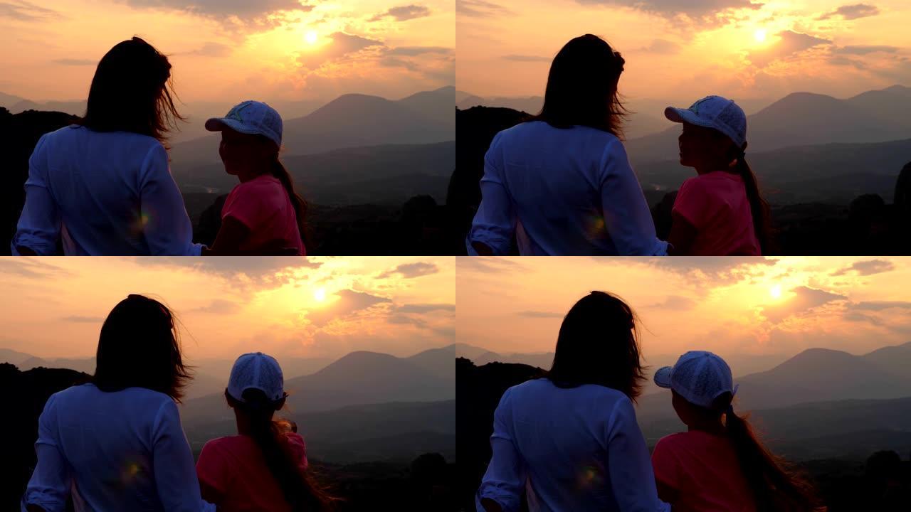 在山里日落的背景下，一个女人和一个十几岁的女孩的轮廓。游客在夏天欣赏希腊梅泰那山的日落