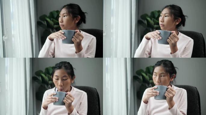 亚洲女孩在灰色马克杯里喝热巧克力，在雨天在家看着窗外，生活方式理念。