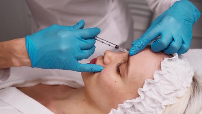 医生美容师在美容院中进行了恢复活力的面部注射程序，以收紧和抚平美丽的年轻女性脸上的皱纹。美容护肤
