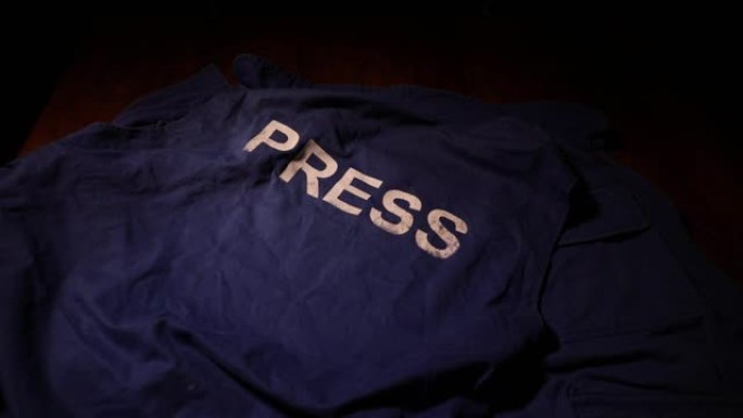 新闻自由和新闻概念。蓝色记者背心在黑暗中与背光和雾。麦克风和手铐。有选择性的重点