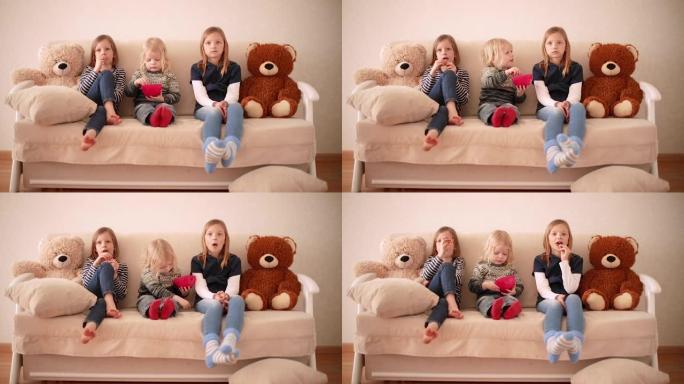 有趣的小男孩 (3岁) 和姐姐 (8岁和9岁) 一起看动画片。兄弟姐妹坐在沙发上吃饼干
