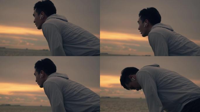疲惫的亚洲运动员在夏天美丽的日落期间在海滩上锻炼锻炼后屏住呼吸。