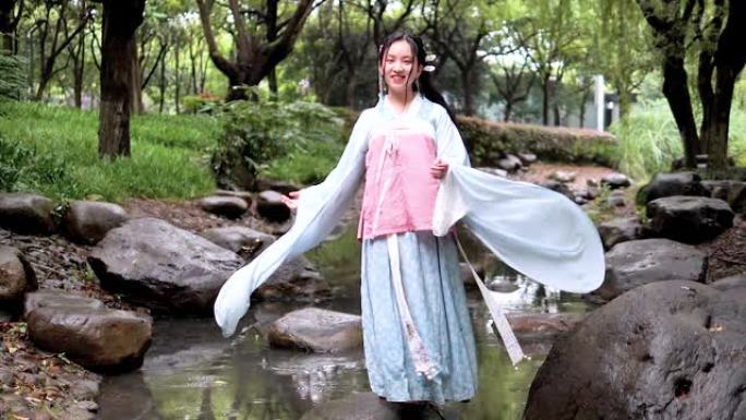 汉服的中国年轻女孩在雨天在溪流中的岩石上旋转。超级慢动作镜头。