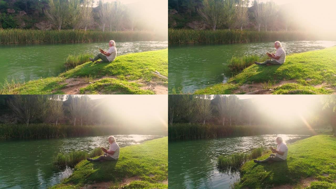 老人读书坐在河边的草坪上