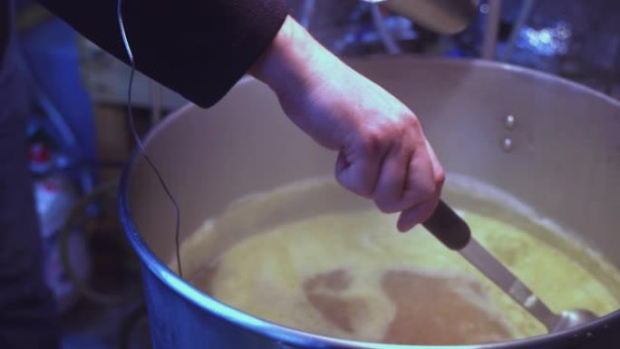 在小型地下室家庭啤酒厂自制酿造。一个人正在向麦芽汁中添加原料，麦芽汁在大锅中沸腾。