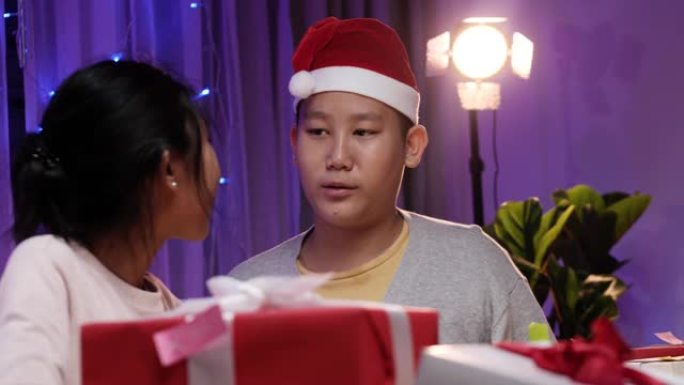 快乐的亚洲孩子戴着圣诞老人的帽子，为圣诞灯背景的家庭派对准备礼品盒和贺卡。