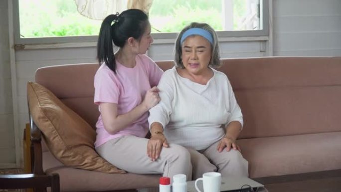 亚洲小女儿在家沙发上与年长的母亲交谈和按摩。老妈患病有少妇照顾