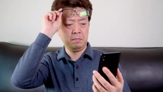 亚洲中年男性试图在手机上阅读一些东西。老花眼，近视。