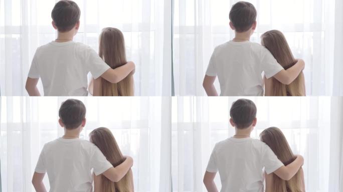 高加索女孩把头放在男孩肩膀上的背景图。孩子们一起站在窗前向外看。初恋，安慰，幸福。