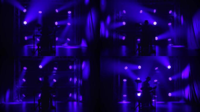 男性鼓手音乐家在黑暗的工作室里在蓝色灯光的背景下演奏乐器。摇滚乐队在舞台上的音乐会，鼓。剪影。慢动作