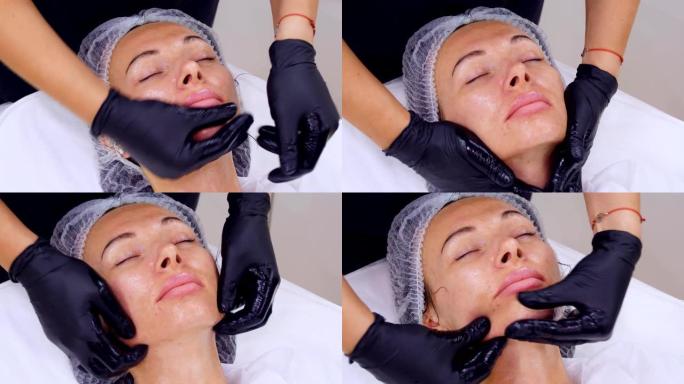 特写，美容师，戴着黑色医用手套，在美容诊所或美容院使用特殊的美容凝胶对女性进行护肤程序，面部按摩