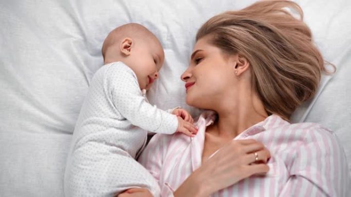 快乐的妈妈和宝宝一起躺在床上，感受爱和温柔。红色相机上的中等镜头