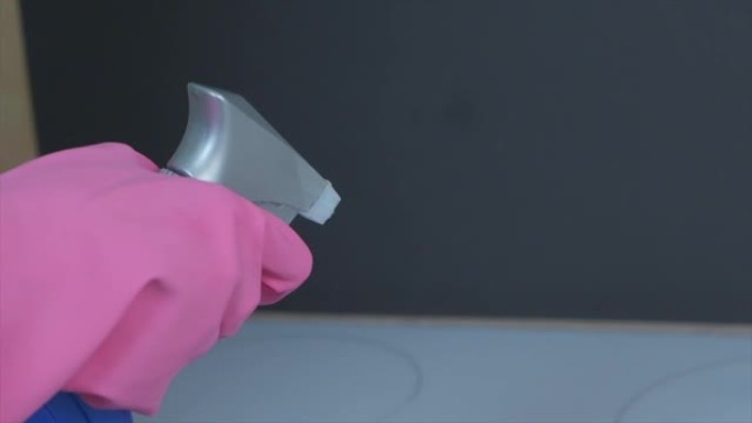 双手戴着乳胶粉色手套，在炉子上喷洒清洁剂。