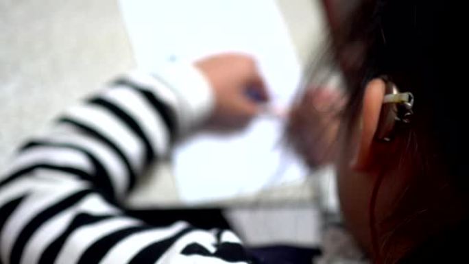听力损失的女孩在做作业。主题在右边。穿着条纹衣服。右手拿着铅笔。