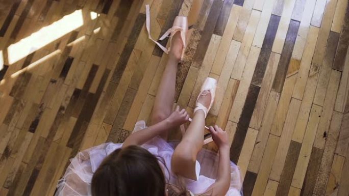 顶视图。芭蕾舞女演员将鞋子换成特殊的芭蕾舞鞋，白色的脚尖鞋，带芭蕾舞丝带的蕾丝。穿着白色短裙的年轻芭