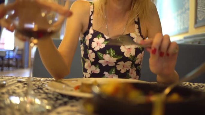 烤土豆、肉、西红柿、莳萝。在餐馆桌子上的盘子里。在一杯酒的背景下，一个女人吃东西，
